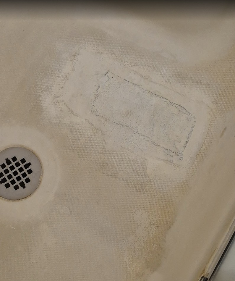 Stained, patched fiberglass shower pan before refinishing in Springfield, MO
