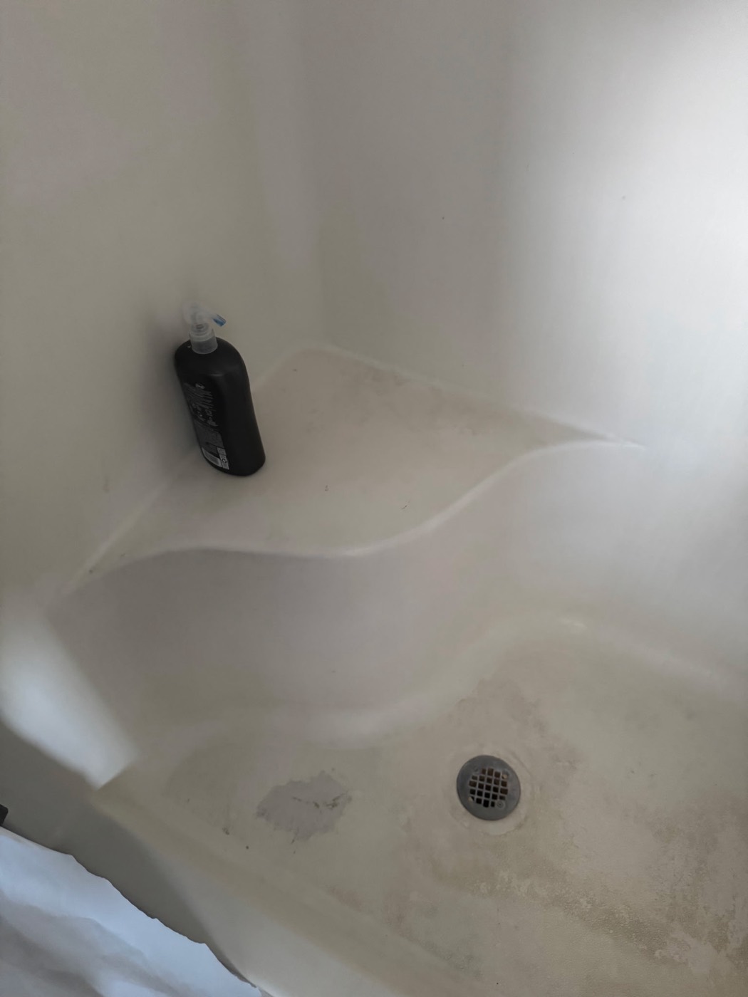 Fiberglass shower stall with a worn, damaged floor before